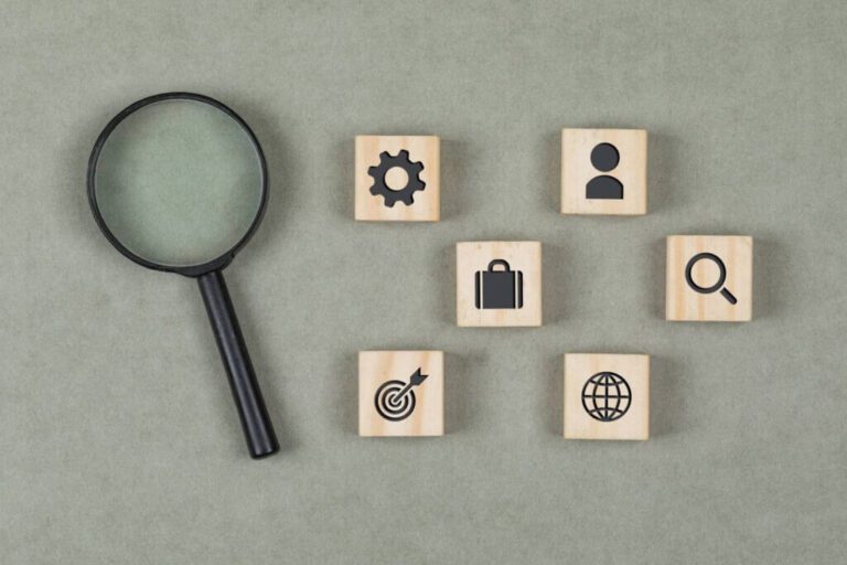 financial-concept-with-wooden-cubes-magnifying-glass-grey-background-flat-lay-1-1-1024x682